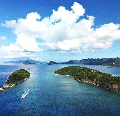 St John boat charters aerial view: a boat leaving a white wake between two green islands near st john, USVI