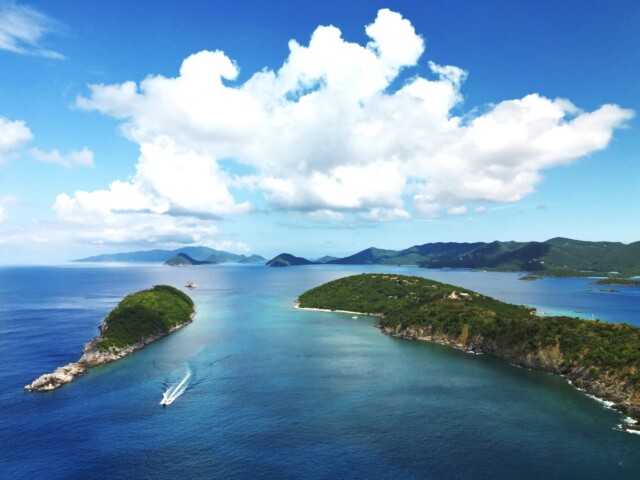 St John boat charters aerial view: a boat leaving a white wake between two green islands near st john, USVI