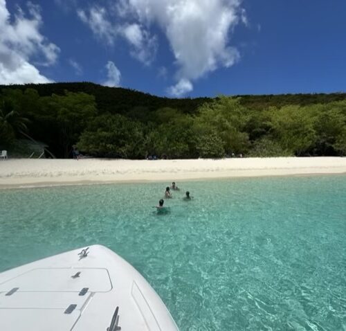Swimmers in turquoise water off an empty white sand beach in St John USVI, seen from the bow of a private st john boat charter