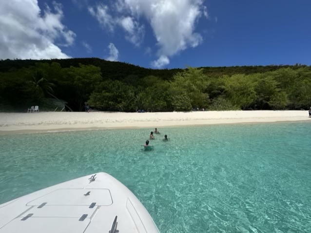 Swimmers in turquoise water off an empty white sand beach in St John USVI, seen from the bow of a private st john boat charter