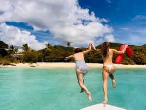 Two friends jumping from a boat bow into turquoise water off a white sand beach, St John USVI