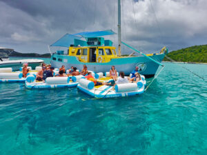 Guests relaxing on floating docks beside the Pizza Pi VI boat in turquoise water near St John, USVI