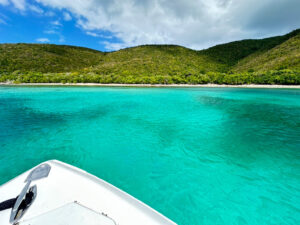 Boat bow anchored in a turquoise bay below green hills in Virgin Islands National Park, St John USVI