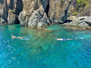 Two snorkelers swimming in clear water beside a rocky cliff shoreline in the Virgin Islands national park, St John USVI